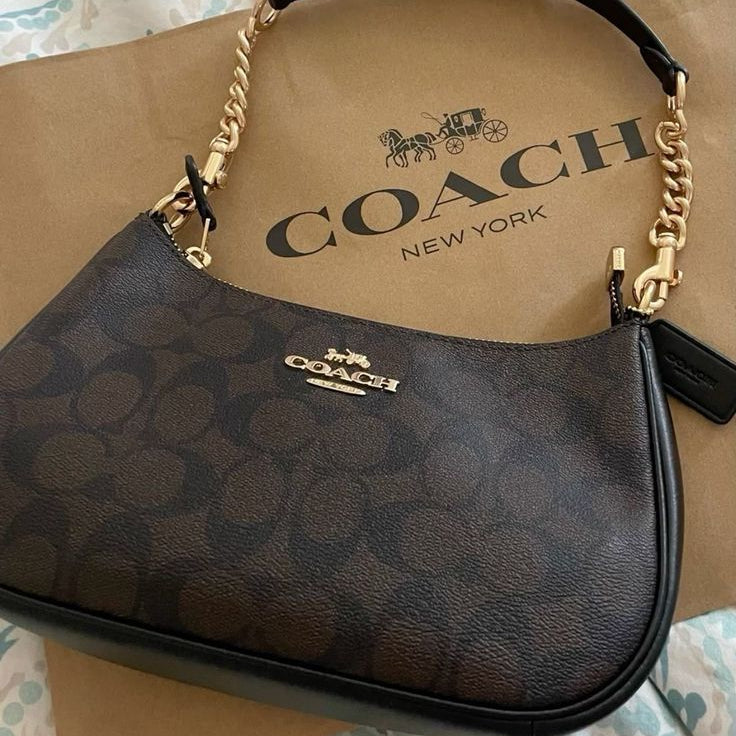 Coach handbag with gold chain strap on a Coach branded paper bag.